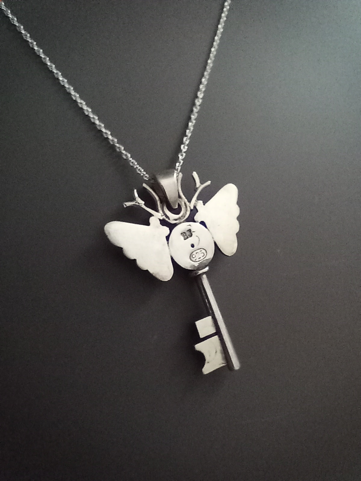 Silver andmoth key pendant necklace on a dark background. The piece deer antlers as antennas. Stamped BJ for designer Brydie Jayne and 925 for Sterling Silver 