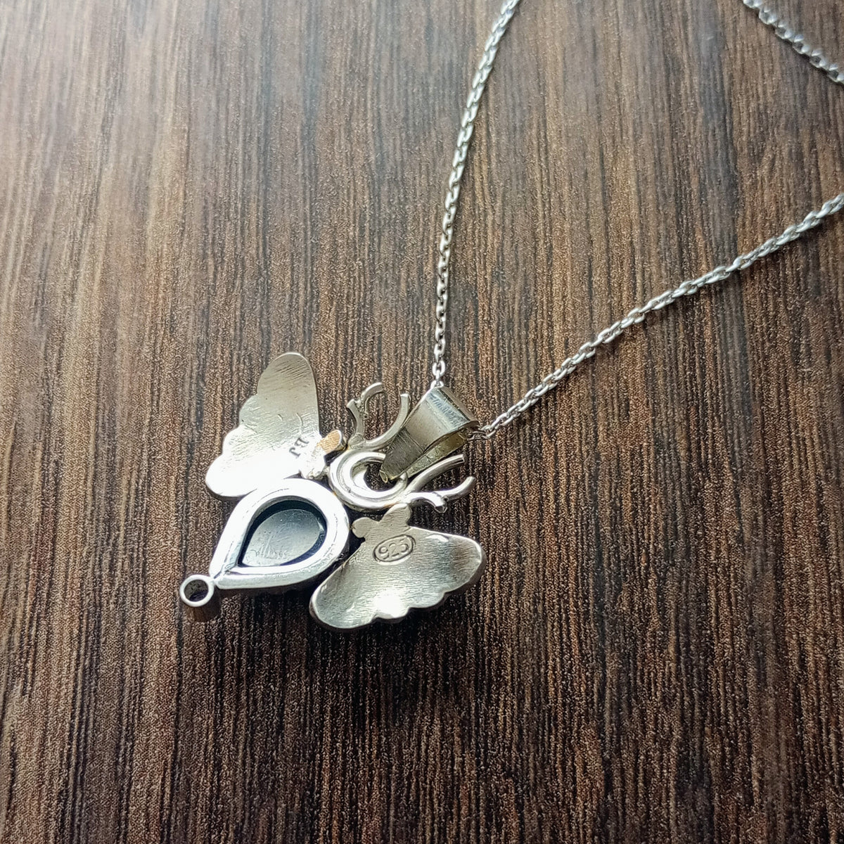 Back of Sterling Silver Moth Pendant featuring Rose cut dark blue sapphire and iolite. Detailed moth wings are made up of two months meeting at top where deer antlers are in place of antennas. Stamped BJ for designer Brydie Jayne and 925 for Sterling Silver.