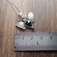 Silver Moth composed of two moth around an inverted pear shaped dark blue sapphire with antlers in places of antennas. Displayed on a wood look background with ruler for scale.