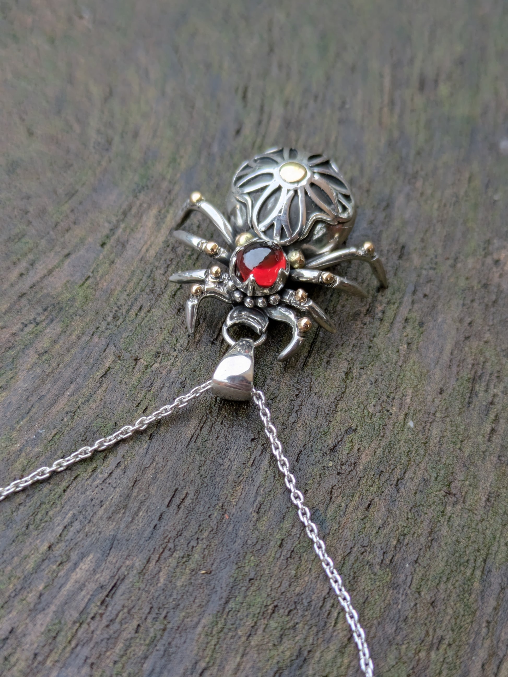Sterling Silver and 9ct yellow Gold spider pendant featuring a gothic rose window inspired design and a garnet cabochon as the head.