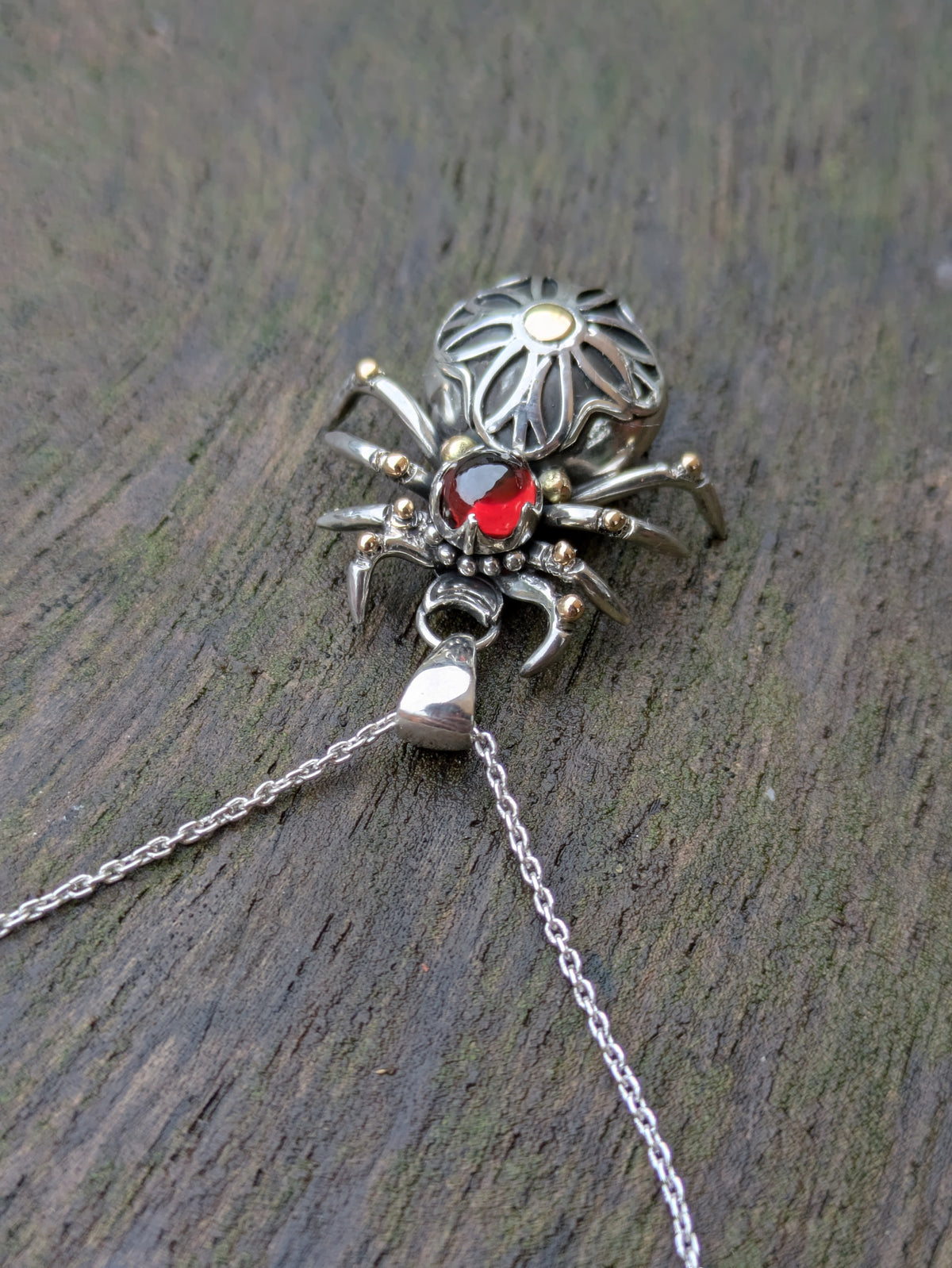 Sterling Silver and 9ct yellow Gold spider pendant featuring a gothic rose window inspired design and a garnet cabochon as the head.