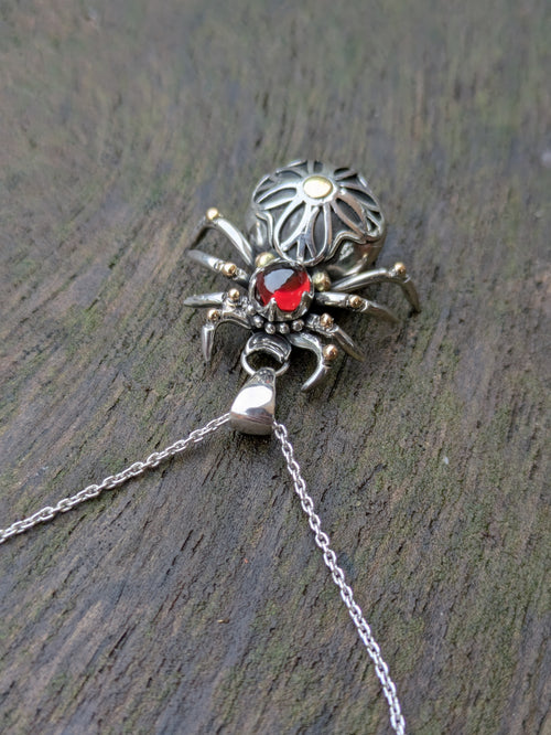 Sterling Silver and 9ct yellow Gold spider pendant featuring a gothic rose window inspired design and a garnet cabochon as the head.