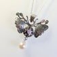 A silver moth pendant made up of two months meeting at the top surrounding a claw set amethyst cabochon with a rope twist around it. The moth has antlers like a deer that include a lead motif and two small peridot stones. A pearl dangles from the tail of the moth and the whole piece is displayed on a silver chain with a white background.