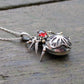 Side view of a gothic rose window inspired spider pendant made from Sterling Silver and 9ct yellow Gold featuring a blood-red garnet cabochon as the head.