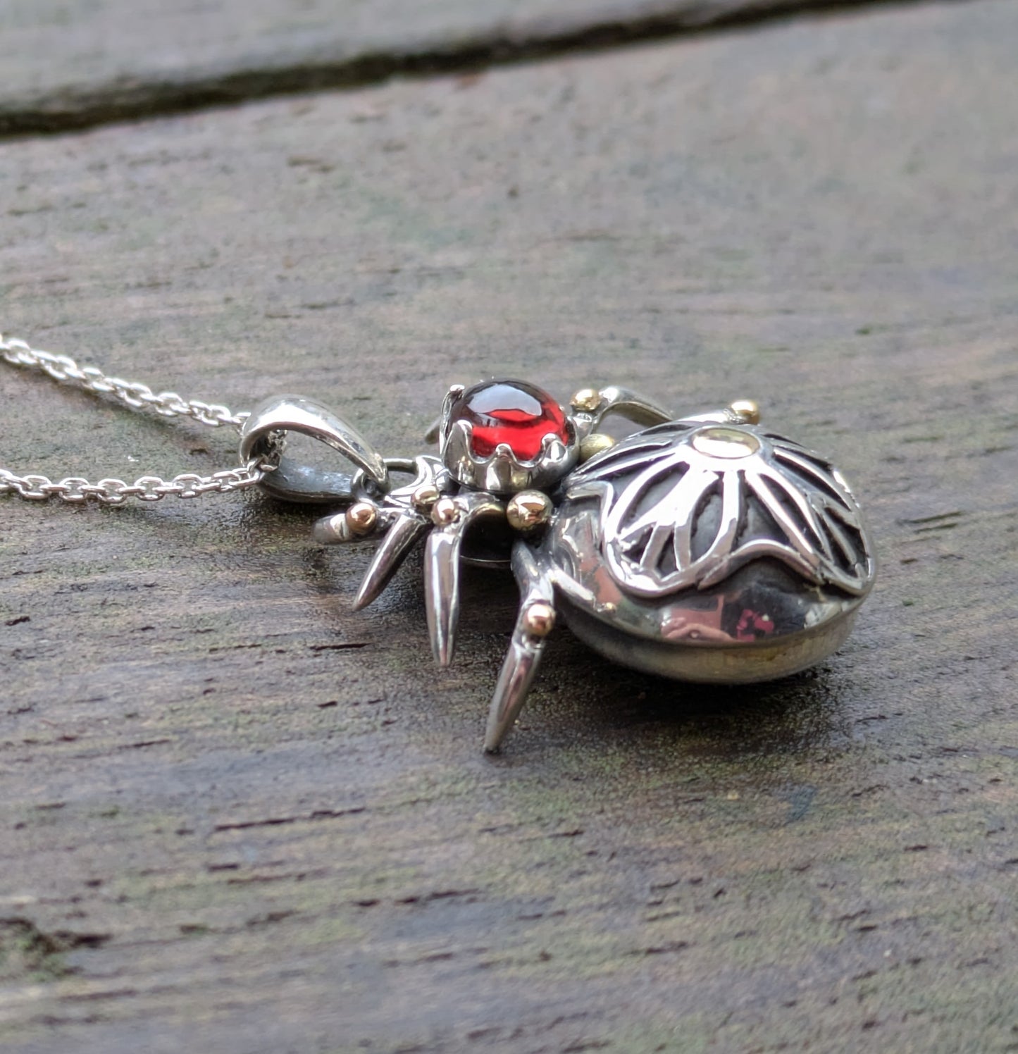 Side view of a gothic rose window inspired spider pendant made from Sterling Silver and 9ct yellow Gold featuring a blood-red garnet cabochon as the head.