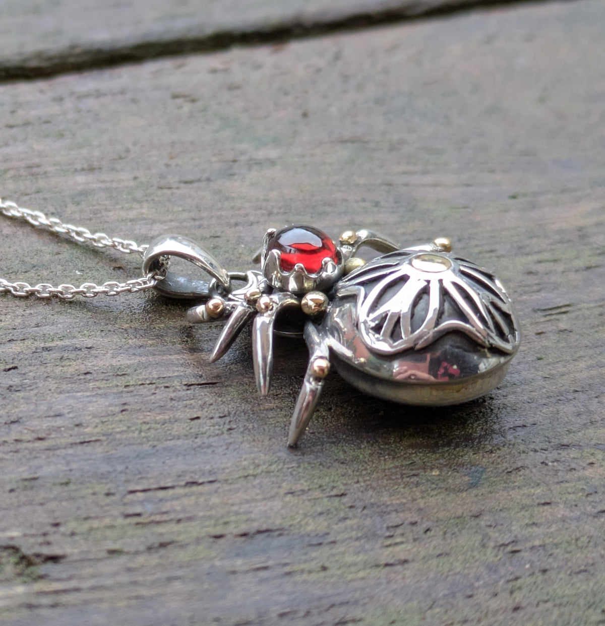Side view of a gothic rose window inspired spider pendant made from Sterling Silver and 9ct yellow Gold featuring a blood-red garnet cabochon as the head.