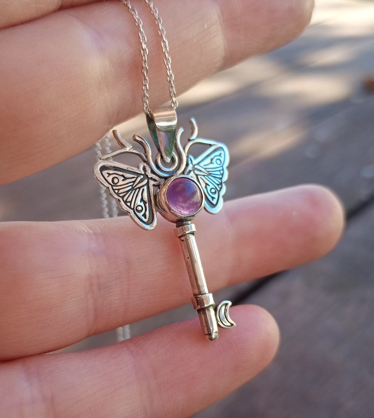 Silver moth key necklace with a purple gemstone held in hand
