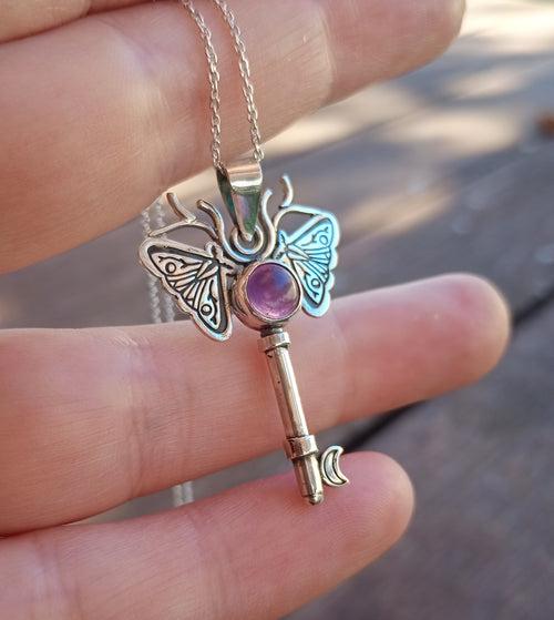 Silver moth key necklace with a purple gemstone held in hand