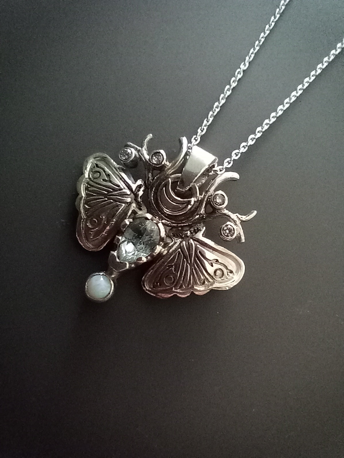 Sterling Silver Moth Pendant featuring Aquamarine, white opal and cubic zirconia. Detailed moth wings are made up of two months meeting at top where deer antlers are in place of antennas.