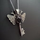 Silver and onyx moth key pendant necklace on a dark background. The piece has moon and a star on the key parts and deer antlers as antennas .