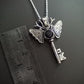 Silver and onyx moth key pendant necklace on a dark background. The piece has moon and a star on the key parts and deer antlers as antennas . Ruler for scale.
