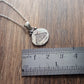 Oval shaped silver pendant with aged appearance stamped with moth design. Accented with a moon at top. Displayed on wood look background with ruler for scale.